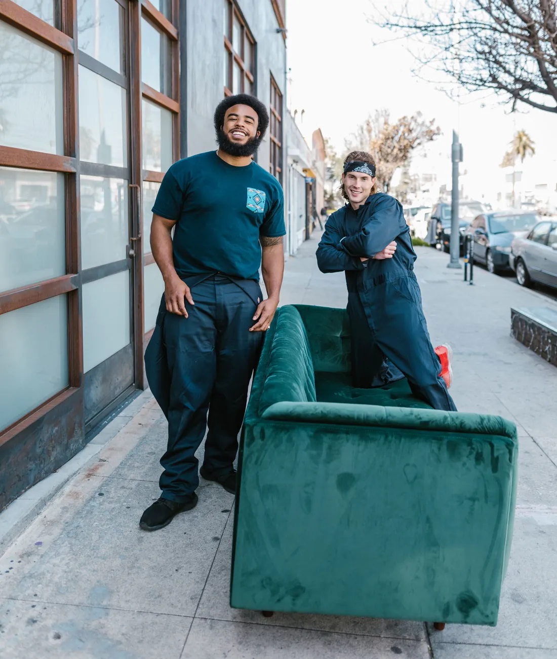 Two junk removal crew members with an old green sofa on the sidewalk, ready to haul it away