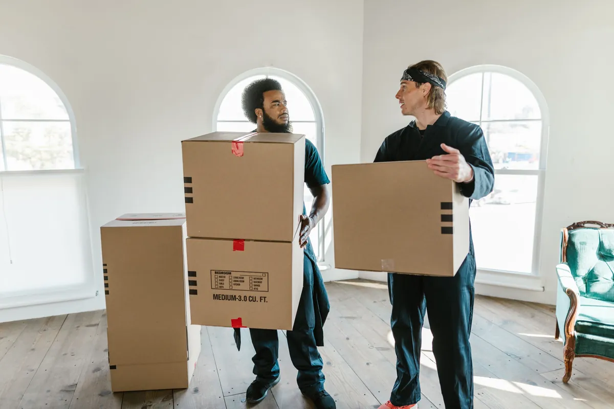 Two haulers carrying stacked moving boxes out of a room